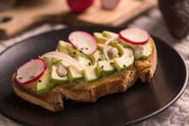 Close up view of toast with avocado and radishes on plate — Stock Photo