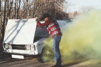 Bearded man opening hood of smoking broken vintage car in nature. — Stock Photo