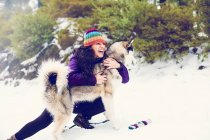 Сміється жінка обіймає собаку в снігах — стокове фото