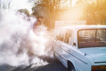 Бородатый мужчина открывает капот дымящегося винтажного автомобиля на природе . — стоковое фото