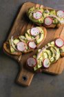 Toast with avocado and radishes on wooden board — Stock Photo