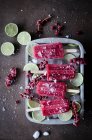 Vista dall'alto del ghiacciolo rosso su bastoncini serviti con pezzi di lime in contenitore . — Foto stock