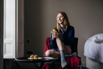 Sorridente donna bionda seduta in poltrona con coppa a casa — Foto stock
