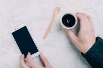 Crop male hands holding black coffee in disposable cup and smartphone — Stock Photo