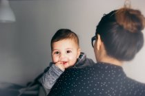Entzückender Junge blickt Mutter über die Schulter in die Kamera — Stockfoto