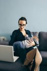 Brunette woman sitting with sleeping child on hands and browsing laptop — Stock Photo