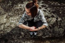 Frau mit Brille sitzt an Steinen und schaut zur Seite — Stockfoto