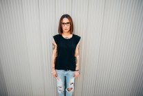 Stylish young woman standing at metal wall and looking at camera — Stock Photo