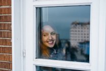 Усміхнена блондинка дивиться через вікно — стокове фото