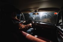 Man in hat driving car with headlights at night. — Stock Photo