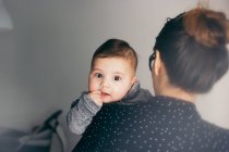 Adorable niño mirando a la cámara mientras está sentado en las manos de la madre - foto de stock