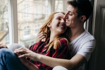 Happy couple hugging on window sill and looking at each other — Stock Photo