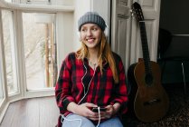 Fröhliche blonde Frau, die zu Hause mit Smartphone Musik hört — Stockfoto