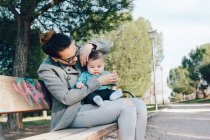 Fröhliche Frau mit Kind an der Hand auf Parkbank — Stockfoto