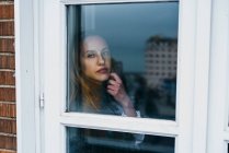 Serena mulher loira posando atrás da janela — Fotografia de Stock