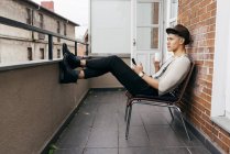 Человек с чашкой и смартфоном сидит на балконе — стоковое фото