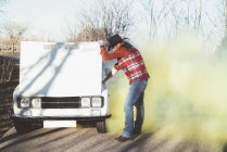 Взрослый мужчина с бородой открывает капот дымящегося автомобиля в солнечной природе . — стоковое фото