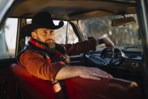 Бородатий чоловік в капелюсі позує в старовинній машині — стокове фото