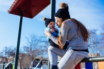 Mãe alegre sentada e brincando com o filho da criança no playground . — Fotografia de Stock