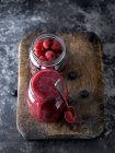 Jar with red fruit smoothie and spoon on wooden board. — Stock Photo