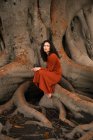 Vue latérale de la femme brune assise sur de grandes racines — Photo de stock