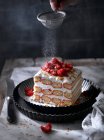 Crop hand powdering sweet berries on cream cake — Stock Photo
