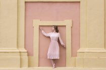 Pretty young woman in pink dress posing at pink facade — Stock Photo