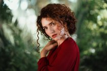 Curly woman in red dress and posing sensually on green. — Stock Photo