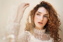 Curly  woman in white lace dress holding small crystal on chain — Stock Photo