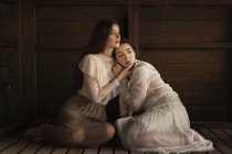 Two brunettes sitting in tender embrace on wooden floor of cabin — Stock Photo