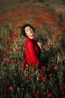 Morena seductora con rizos posando en el campo con flores de amapola en flor con los ojos cerrados . - foto de stock