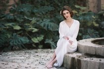 Femme tendre en robe blanche assise à la fontaine dans le parc — Photo de stock