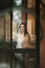 Hübsche Frau in weißem Kleid posiert vor der Tür und blickt in die Kamera — Stockfoto