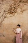 Женщина, стоящая у стены с сухой листвой — стоковое фото
