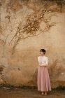 Femme réfléchie posant avec le menton sur la main au mur avec un feuillage sec — Photo de stock