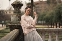 Pensive woman in glasses posing by stone handrail on terrace — Stock Photo