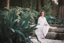 Junge brünette Frau in weißen Kleidern sitzt am Brunnen im Park. — Stockfoto