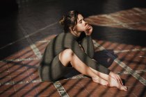 Чуттєва дівчина сидить на підлозі в сонячних променях з підборіддям на руці — стокове фото