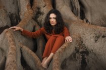 Приваблива брюнетка жінка сидить у корінні великого дерева . — стокове фото