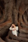 Mulher sentada em raízes de árvore com a cabeça na mão e olhando para a câmera — Fotografia de Stock