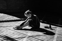 Sinnliches Mädchen, das in Sonnenstrahlen auf dem Boden sitzt und Füße berührt — Stockfoto