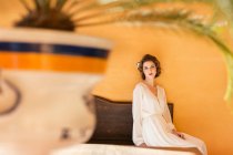 Femme sensuelle en robe blanche assise sur un banc en bois et regardant la caméra — Photo de stock