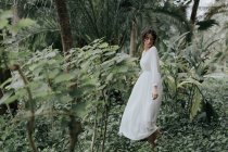 Romantisches Mädchen in Weiß posiert inmitten tropischer Pflanzen mit geschlossenen Augen — Stockfoto