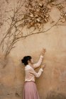 Вид сбоку: женщина ползает руками по стене с сухими ветвями и листьями . — стоковое фото
