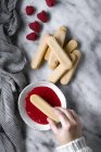 Cosecha hembra mano sumergiendo galletas en mermelada de frambuesa - foto de stock