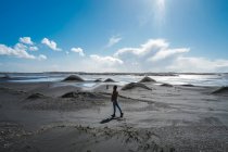 Seitenansicht einer anonymen Person, die an einem menschenleeren schwarzen Sandstrand in Island spaziert — Stockfoto