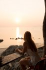 Жінка дивиться на захід сонця на кам'янистому пляжі — стокове фото