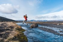 Vista laterale del giovane in abito casual che salta oltre il torrente mentre viaggia attraverso la meravigliosa campagna islandese — Foto stock