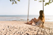 Femme assise sur des balançoires sur la plage — Photo de stock
