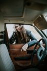 Blick aus dem Auto auf junge attraktive Frau, die sich ans Fenster lehnt und in die Kamera blickt. — Stockfoto